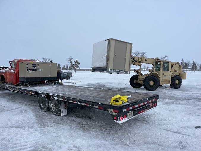 Actual folded ACE shelter being handled by a forklift beside a flatbed trailer in snow